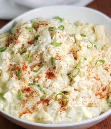 White Round Bowl with Cauliflower Mock Potato Salad, garnished with red paprika and green scallions for color
