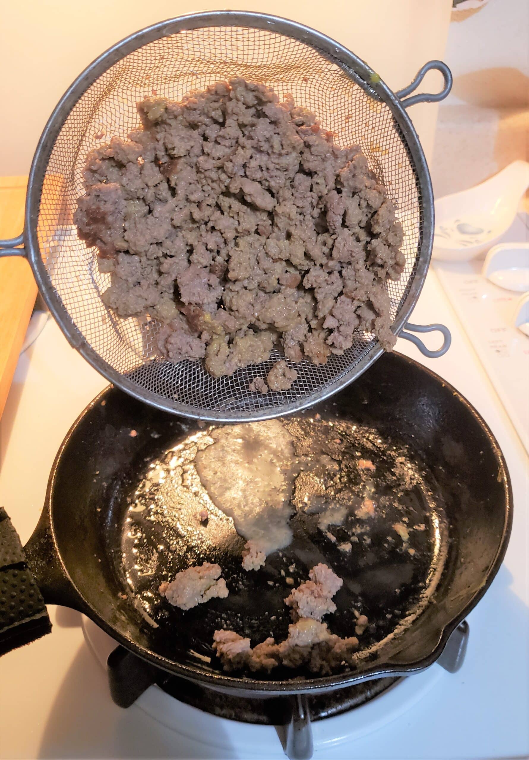 Ground beef in strainer being poured into a hot skillet